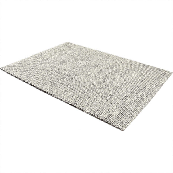 Diagonaal aanzicht van vloerkleed NURA, in de kleur grijs wit gemaakt van wol.